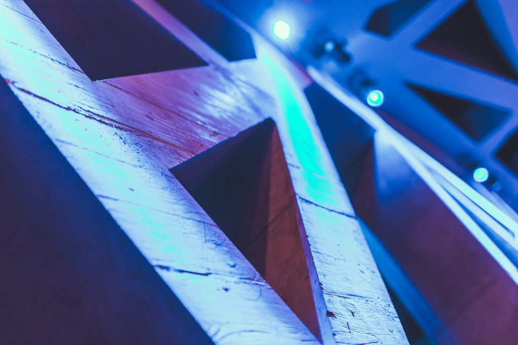 © Sergiu Andrés Diagonal white wooden beams form geometric shapes, lit by blue stage lighting in a dark room with circular spotlights in the background