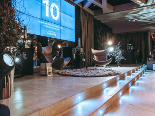 Special Event by Nespresso Stage setup with a large blue digital screen showing '10' and event text, two modern lounge chairs, and a fluffy rug under soft lighting.