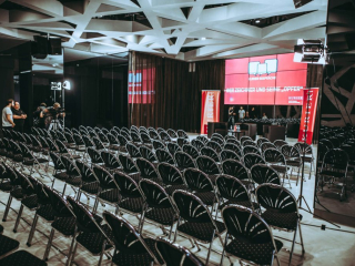 Niklas Stadler wwwniklasstadlerat Rows of black folding chairs facing a red-lit stage screen in a modern event space.
