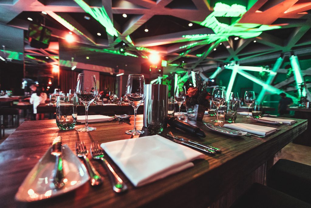 Palais Wertheim Banquet table set for a formal dinner with wine glasses, folded napkins, and a floral centerpiece under vibrant green lighting, in a modern venue.