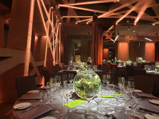 Elegant banquet hall set for a formal dinner with round tables, glassware, and a glass centerpiece bowl in the foreground.
