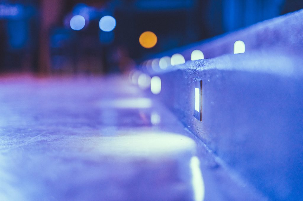 © Sergiu Andrés Close-up of a blue ice rink barrier with an embedded square light, blurred background bokeh.