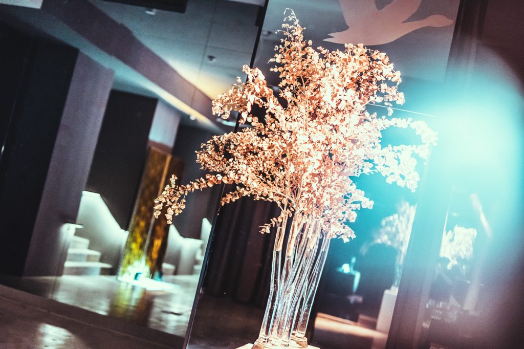 Palais_Wertheim_Galadinner_Speedinvest-8 Tall glass vases with peach-colored dried branches arranged as a centerpiece in a dim, modern interior setting.