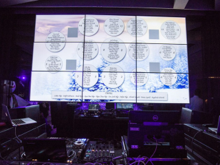 Palais Wertheim Large video wall showing a circular seating chart over a snowy forest background, with DJ mixers and laptops in the foreground under purple lighting.