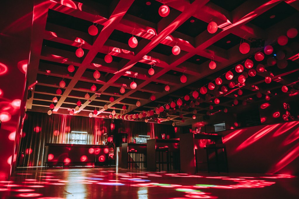 Palais_Wertheim_Schulball_Goethegymnasium-6 Nightclub interior with red hanging spheres and colorful light reflections on the floor and bar area in the back.