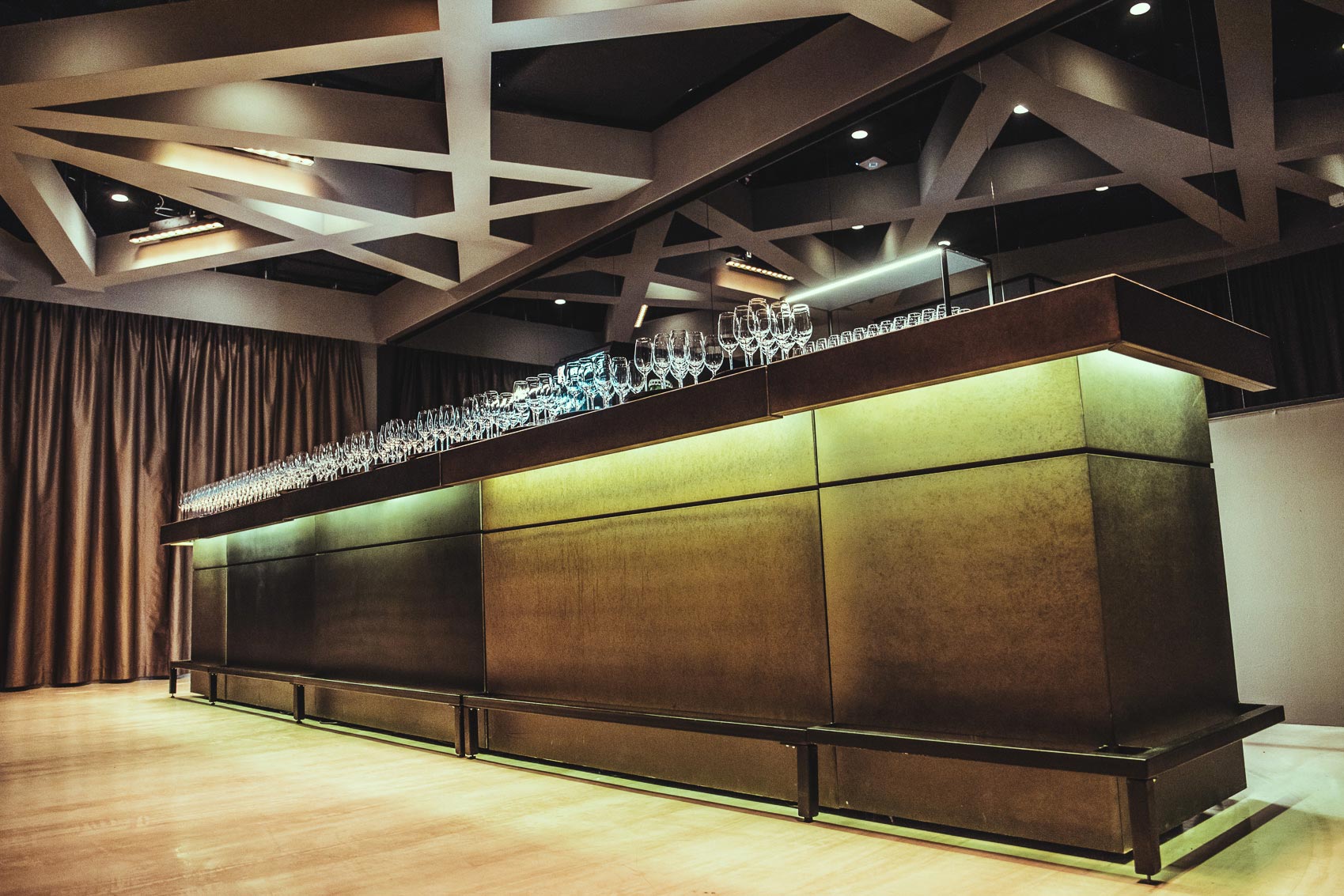 Long modern bar with glassware lined along the top and warm backlit panels in a stylish venue.