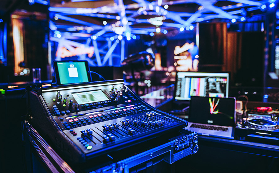 DJ mixing console with illuminated controls and a laptop in a blue-lit nightclub booth