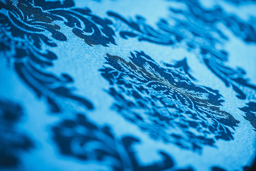 Close-up of a blue damask textile with an ornate floral pattern.
